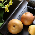 three whole asian pears of various sizes on a black platter with yellow flowers
